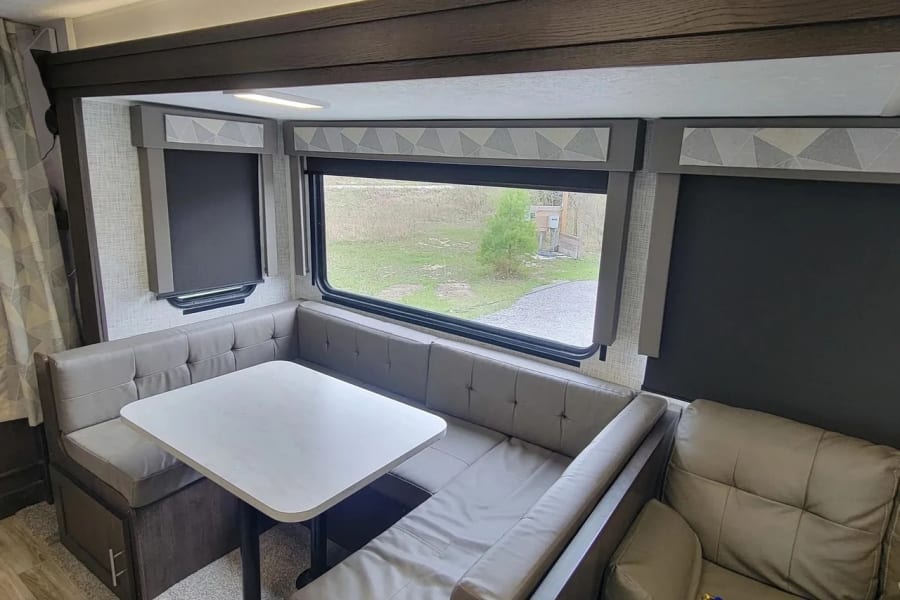RV rental interior: a comfy U-shaped dinette with table and large window, offering an outside view.