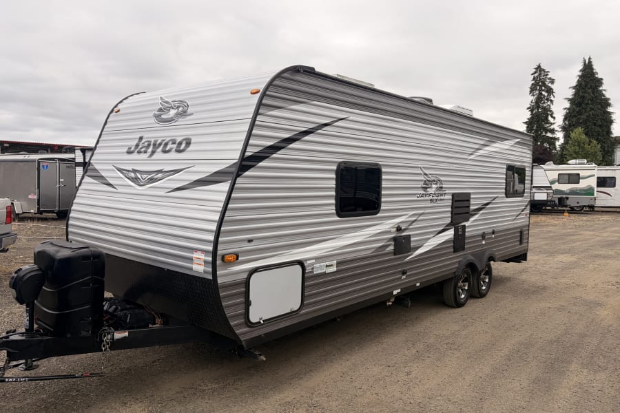 Explore with this Jayco travel trailer RV rental. A gray and black camper on gravel, with a cloudy sky overhead.
