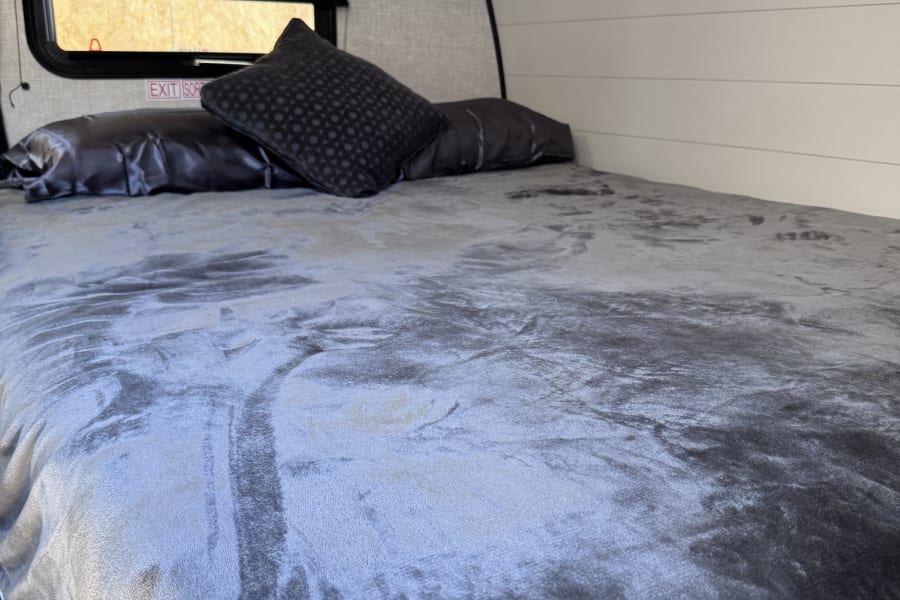 RV rental bedroom with a cozy bed, dark pillows, a window, and an air conditioning unit for comfortable travel.
