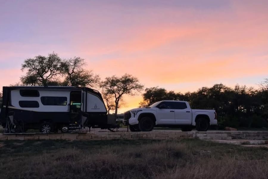 Our RV rental, a modern travel trailer, hitched to a white pickup at a beautiful sunset campsite, ready for adventure.