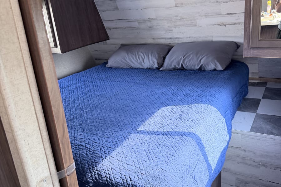 Cozy RV rental bedroom with a blue quilted bed, grey pillows, and light wood-look walls, perfect for travelers.