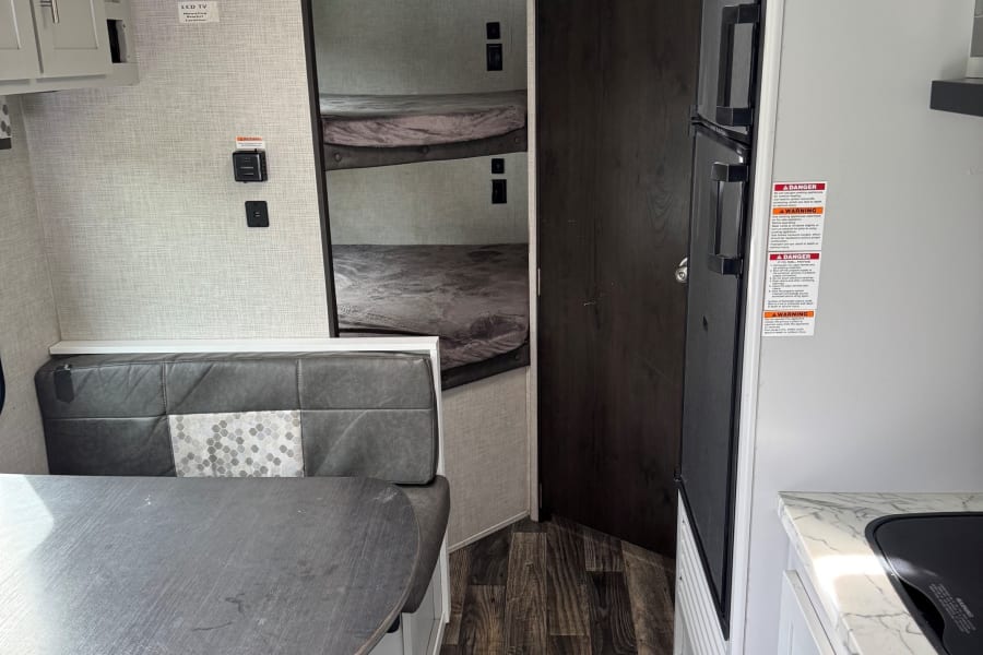 This RV rental offers a practical interior featuring a dinette, bunk beds, and a functional kitchen with a refrigerator.
