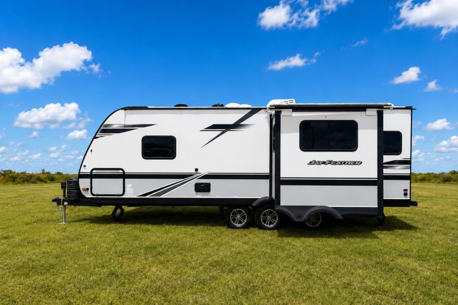 A white Jay Feather travel trailer, ideal for RV rental, parked on vibrant green grass under a bright blue sky.