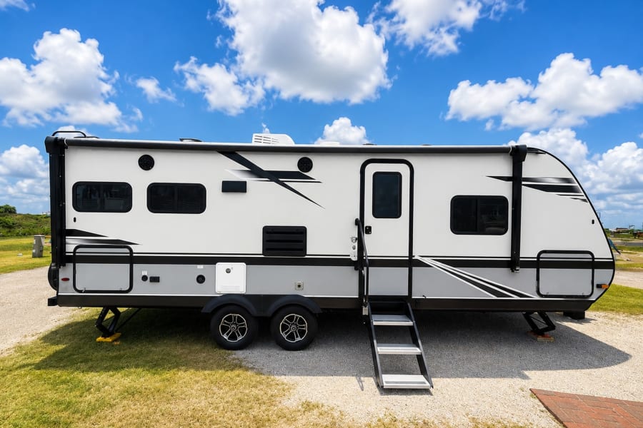 White and grey travel trailer RV rental parked outdoors under a bright blue sky, ideal for your next vacation.