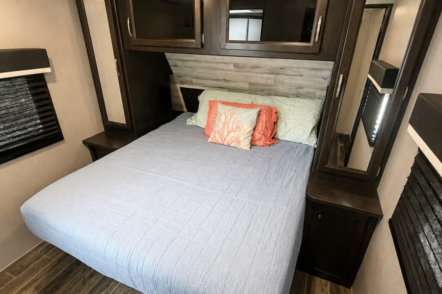 RV rental bedroom interior features a bed, dark wood cabinetry, decorative pillows, and wood-look flooring.