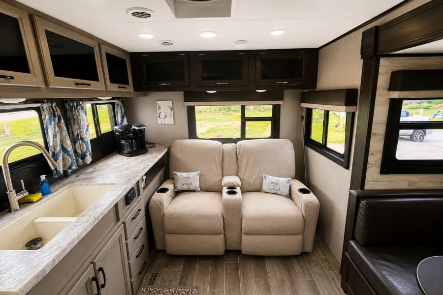 RV rental interior: kitchen with sink & coffee maker, comfy dual recliners, and a dinette sofa. Modern, inviting space.