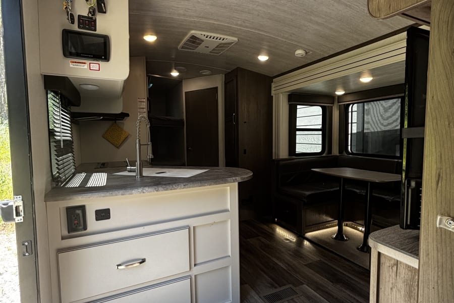 Interior of an rv rental travel trailer, featuring a bright kitchenette with a sink, dinette, and bunk beds in the background.