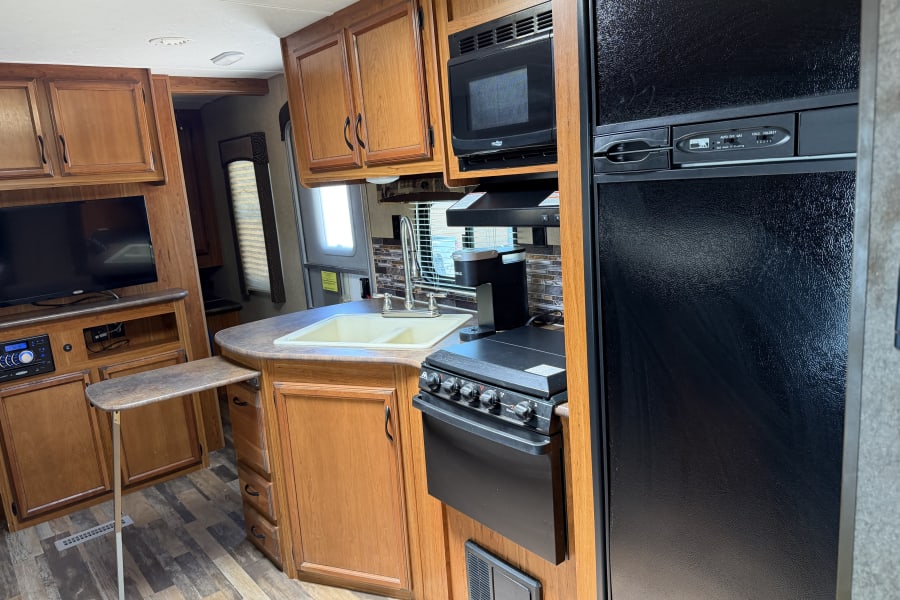 RV rental kitchen area with a sink, microwave, stove, and refrigerator, along with a TV and wood cabinets.