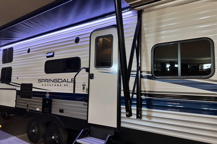 Explore with this RV rental: a Springdale Keystone travel trailer's side with extended awning, LED lights, open door, and steps.
