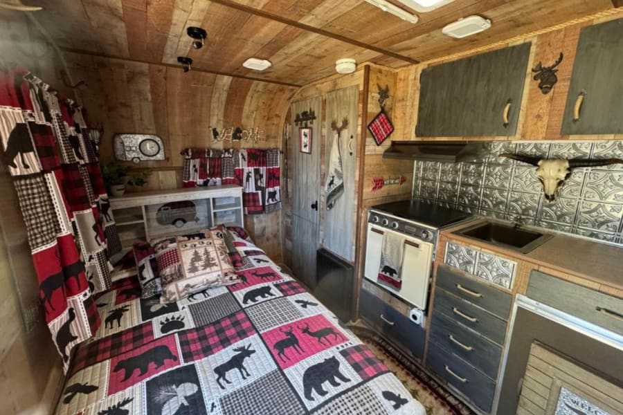 Explore this cozy, rustic RV rental! Wood-paneled interior features a plaid wildlife quilt, compact kitchen, and charming cabin decor.