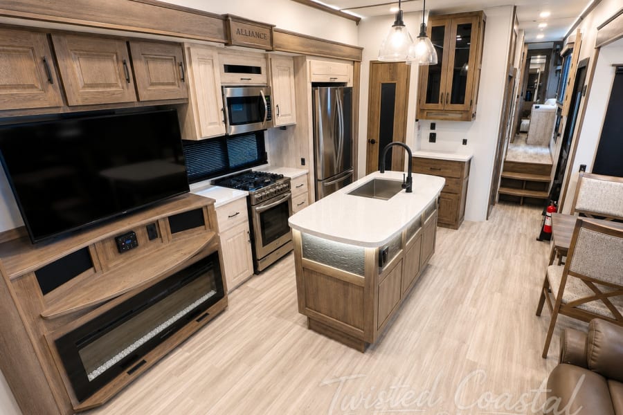 Luxury RV rental interior: well-appointed kitchen, island, living area with TV & fireplace for comfortable adventures.