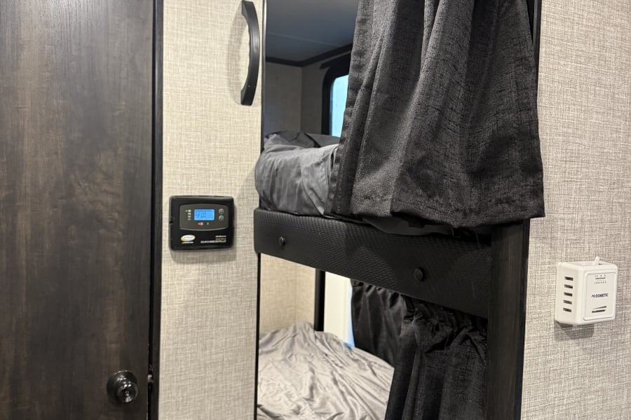 RV rental bunk beds with privacy curtains, a solar charge controller, and thermostat, showing a compact, functional interior.