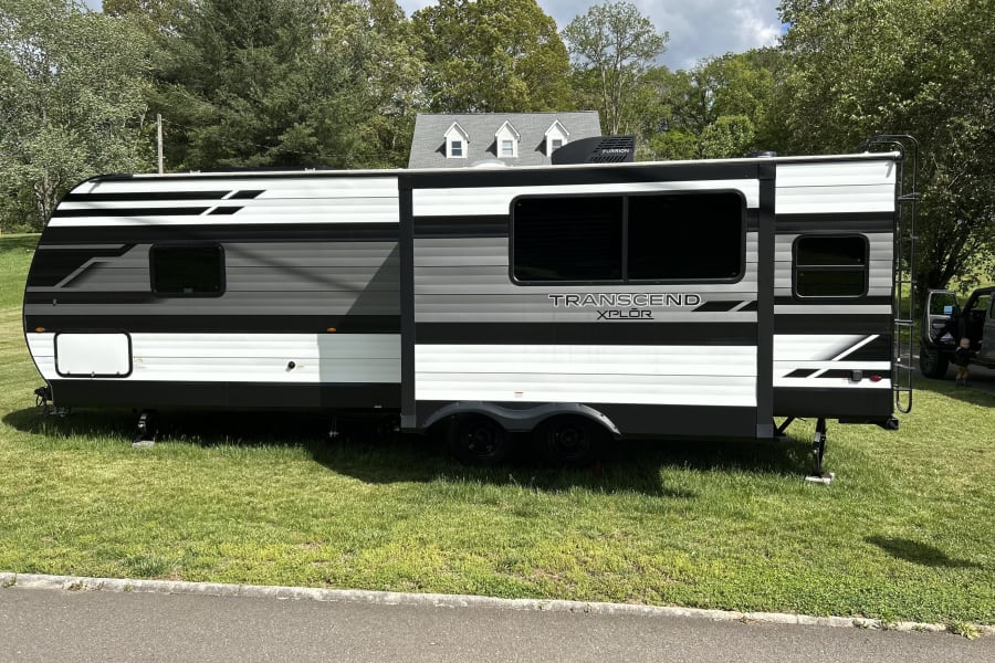 A sleek black, white, and gray Transcend Xplor travel trailer, ideal for your next RV rental, parked on lush grass.