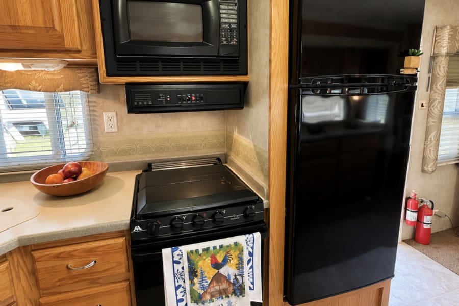 Inside an RV rental, a well-equipped kitchen features oak cabinets, black appliances like a microwave, stove, and refrigerator.
