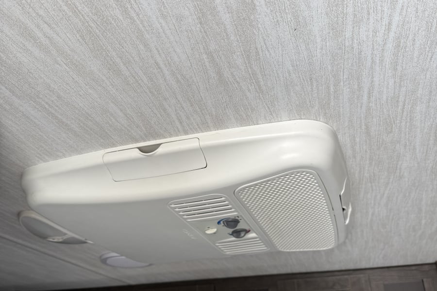 RV rental interior: Ceiling-mounted air conditioner (AC unit) with controls and ventilation above dark wood cabinets.