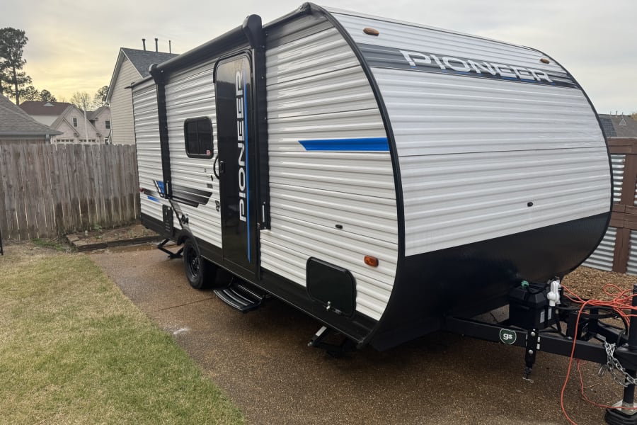 White Pioneer camper, perfect for an rv rental, parked on a driveway. Features black and blue accents.