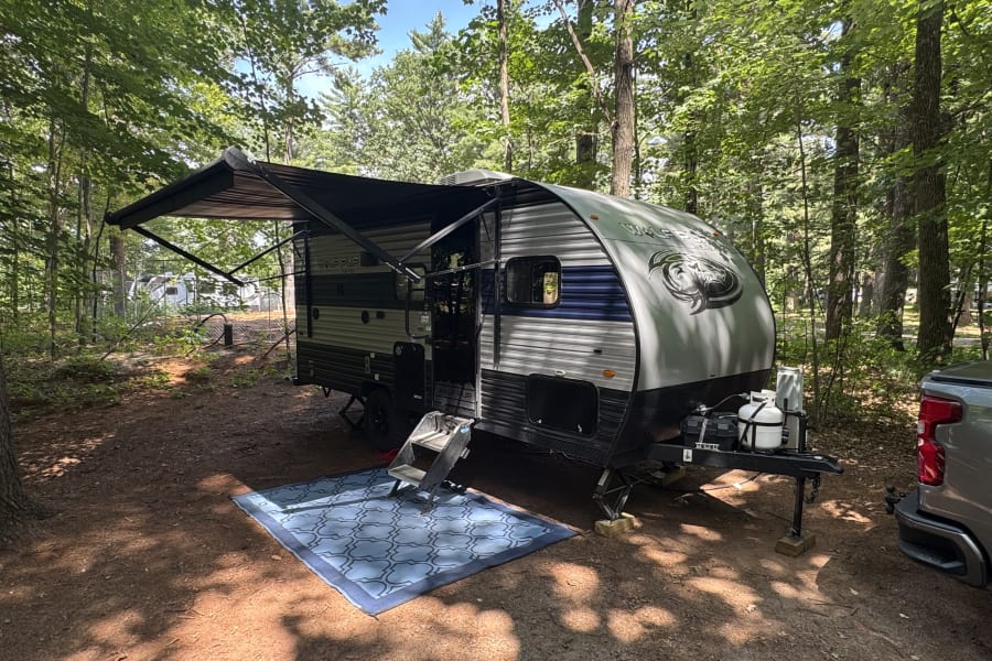 This Wolf Pup RV rental is perfectly set up at a serene wooded campsite, ready for a relaxing outdoor adventure.