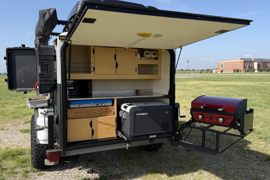 RV rental off-road trailer with open rear kitchen. Features include a Dometic fridge, stovetop, and attached grill.