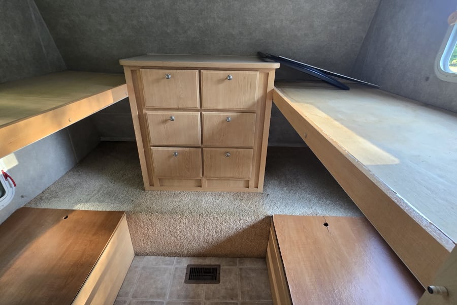 RV rental interior featuring bunk beds, a central dresser with six drawers, and two floor storage compartments.