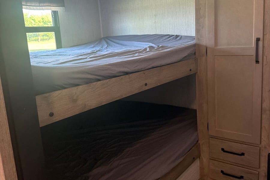 Inside this RV rental: two bunk beds with gray bedding, a window view, and built-in storage.