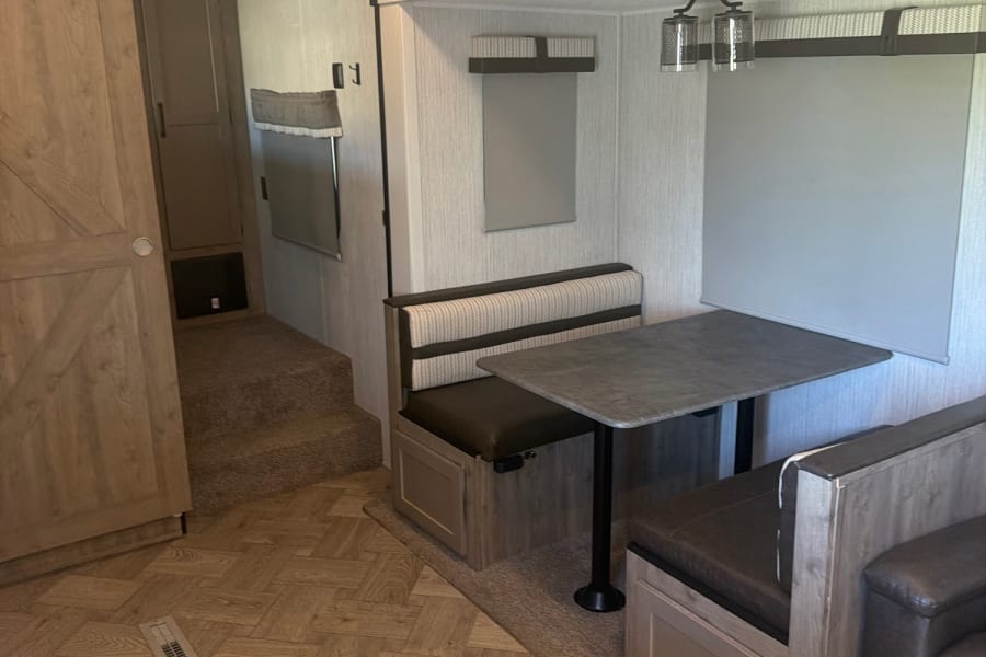 RV rental interior: dining area with upholstered benches & table, leading to a carpeted bunk space.