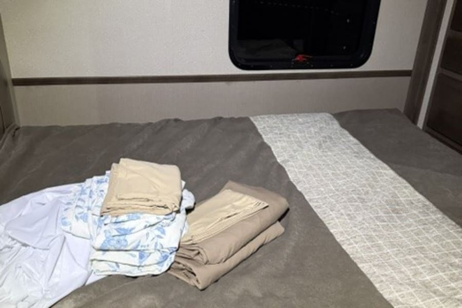 RV rental bedroom with neatly folded linens (beige, floral, white) on the bed. Dark window view suggests night.
