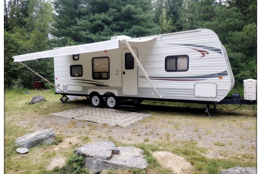 A white travel trailer with an extended awning is set up at a grassy campsite, ready for your next RV rental adventure.