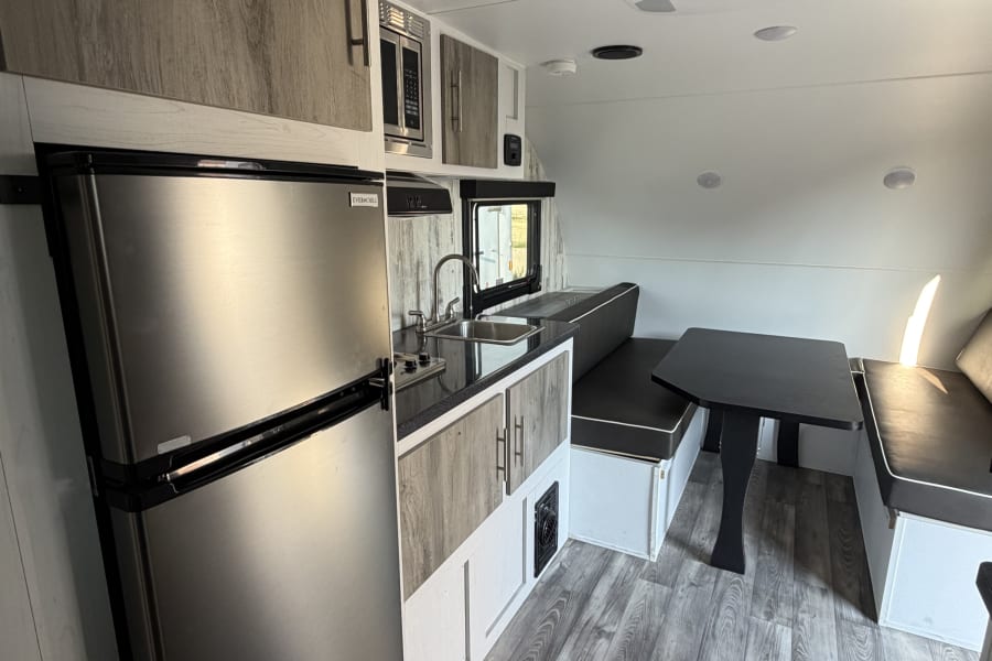 Modern RV rental interior with kitchen, dining area, fridge, microwave, and AC. Features wood-look flooring.