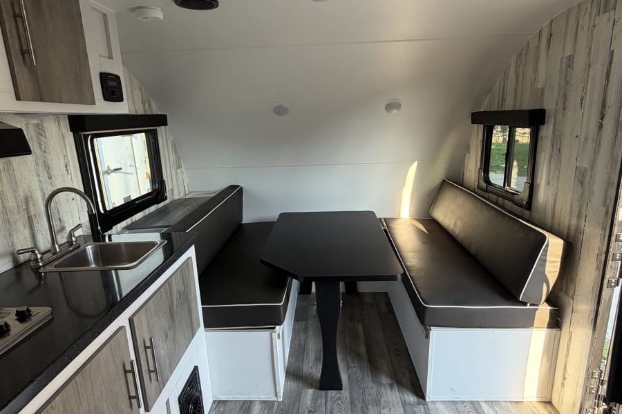 This rv rental shows a bright, modern interior with a dining booth, compact kitchen, and stylish gray wood accents.