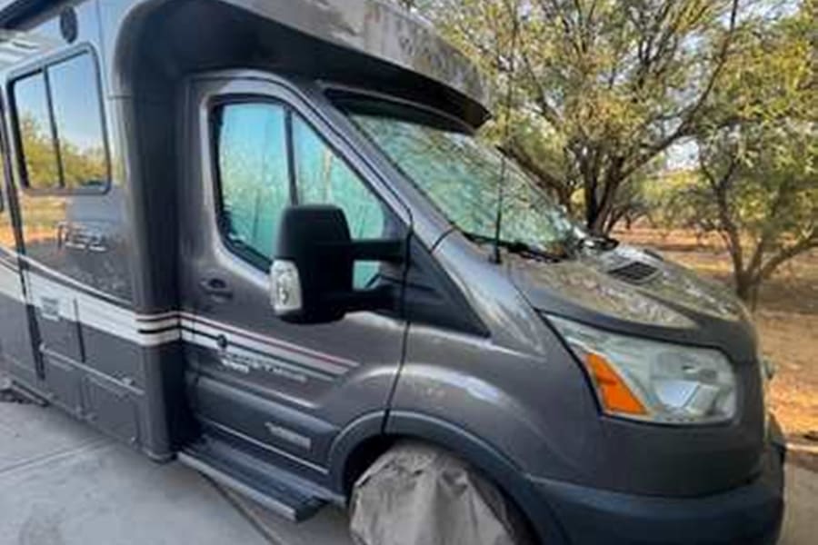 Sleek gray RV rental camper van parked outside. Front wheel covered. Ideal for your next outdoor adventure.