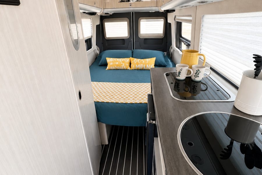 Spacious rv rental interior showing a comfortable bed, compact kitchen, and overhead storage, perfect for your next adventure.