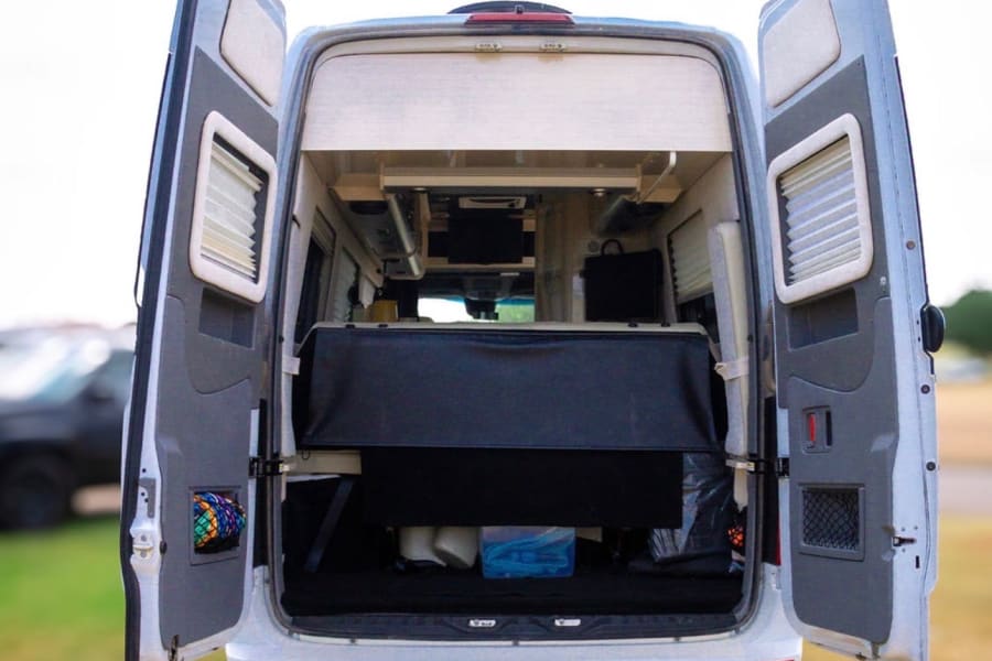 RV rental: Rear doors open on this camper van, revealing its bed, storage, and a glimpse of adventure.