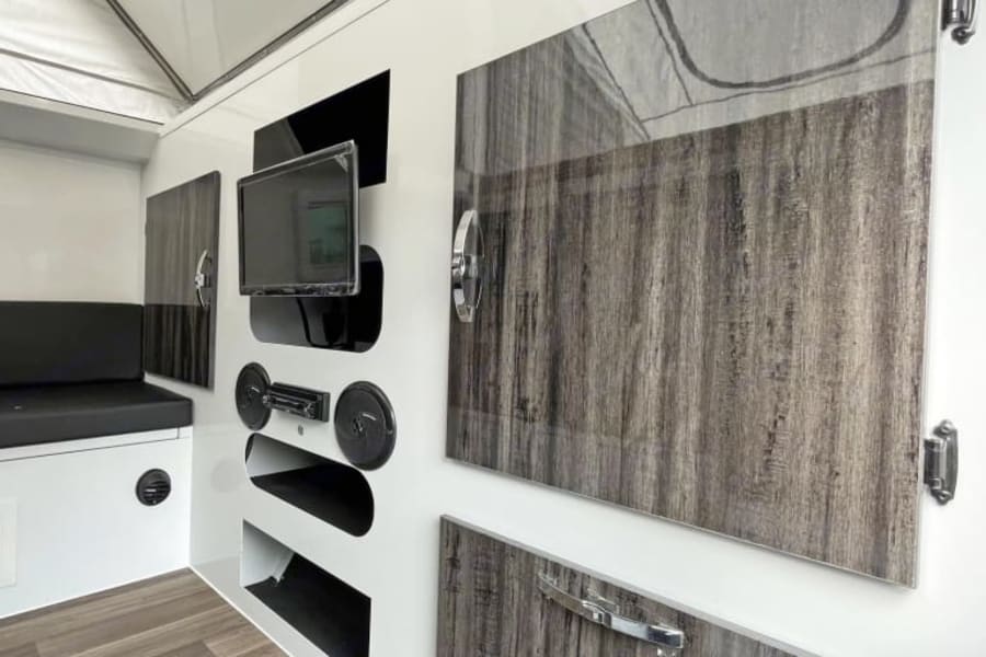 RV rental interior: a pop-top camper's modern design with wall-mounted TV, audio system, bench, and sleek wood-grain cabinets.