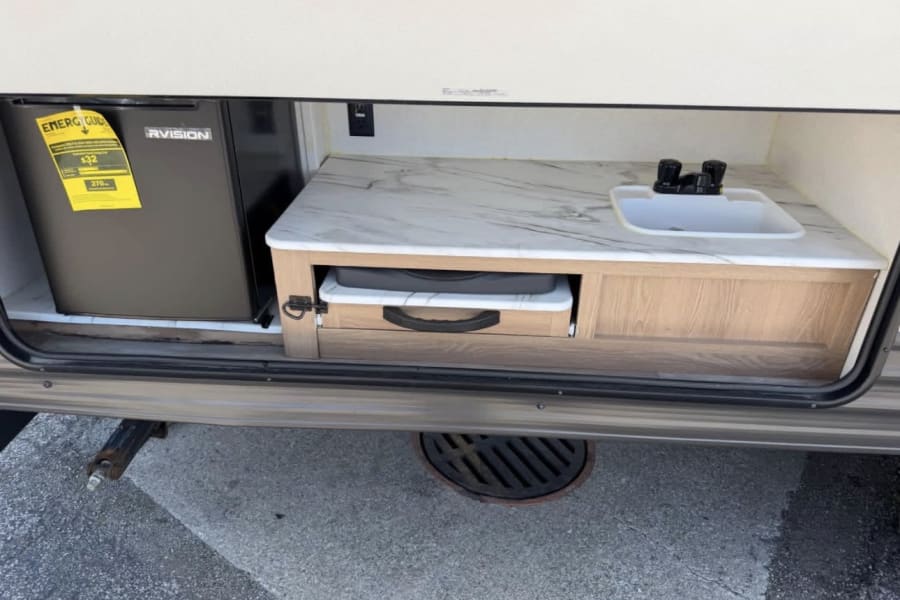RV rental's outdoor kitchen features a mini-fridge, sink, and a pull-out area, ideal for convenient outdoor cooking and camping.