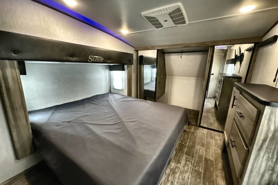 Comfortable rv rental bedroom with a large bed, "Suite" headboard, blue accent lighting, ceiling AC, and mirrored closet.
