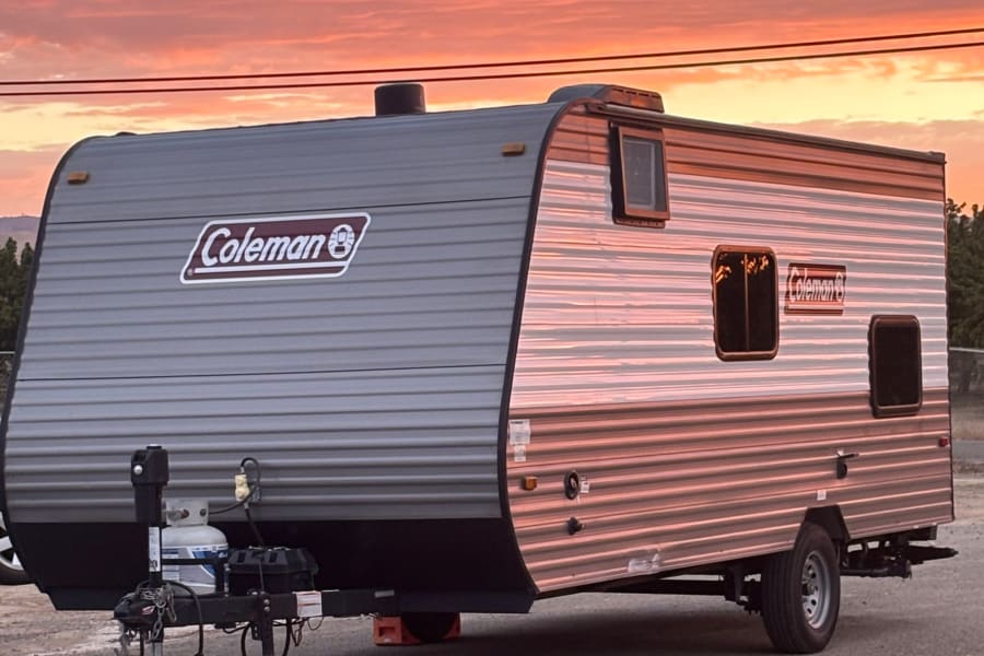 A Coleman RV rental gleams under a vibrant sunset, perfect for camping and road trip adventures.