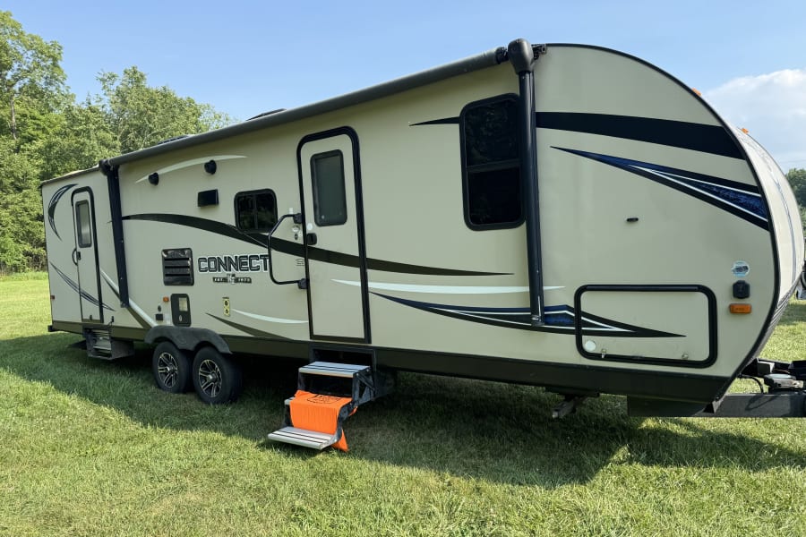 This beige travel trailer RV rental, with an orange step cover, is ready for a scenic camping adventure.