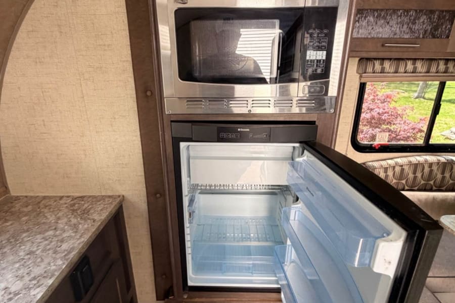 RV rental kitchen: microwave and open Dometic fridge with empty shelves, ready for your next adventure.