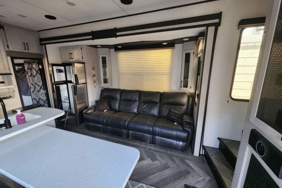 Modern RV rental living space featuring a comfy black leather sofa, kitchen island, fridge, and chic flooring.