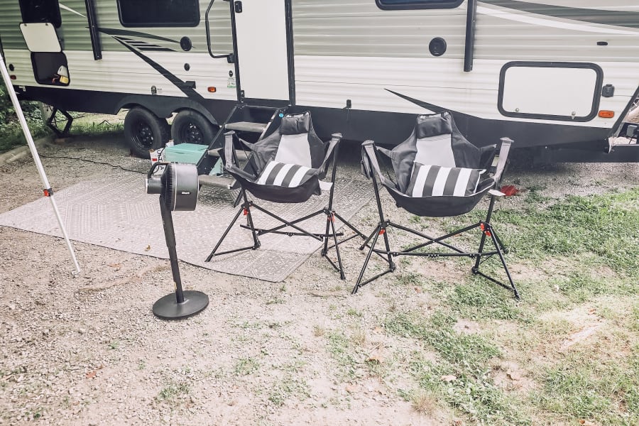 RV rental at a scenic campground with a warm fire pit, comfortable outdoor chairs, and lush trees in the background.