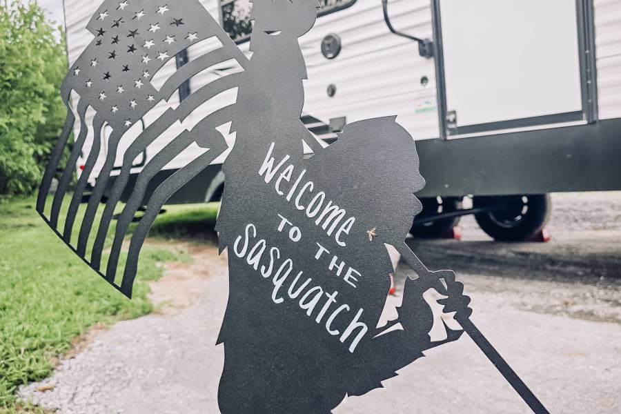 "Welcome to the Sasquatch" Bigfoot sign with American flag, outside a white RV rental.