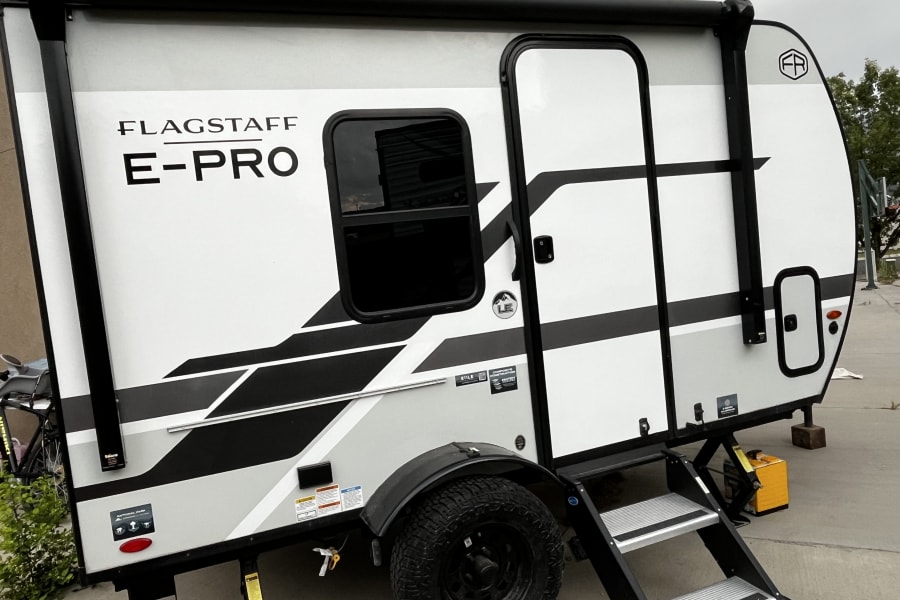 A Flagstaff E-Pro travel trailer, an ideal RV rental for adventures, with bold graphics, off-road tires, and sturdy steps.