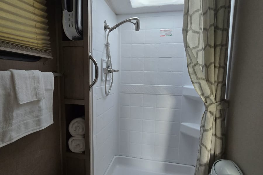 Clean RV rental bathroom with shower, toilet, towel rack, and shelves. Compact and functional space.