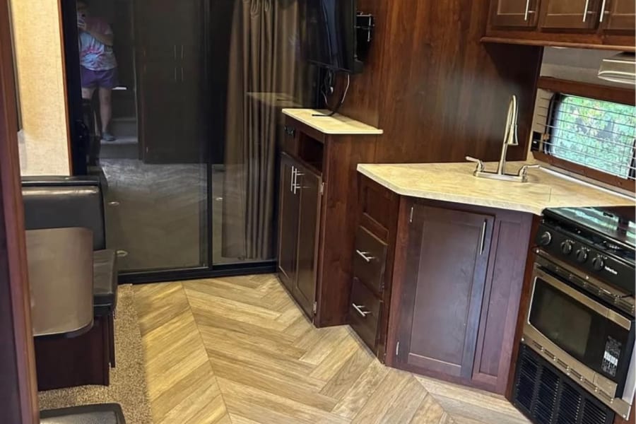 Spacious RV rental with a modern kitchen, dining area, dark wood cabinetry, and herringbone flooring. Ready for travel!