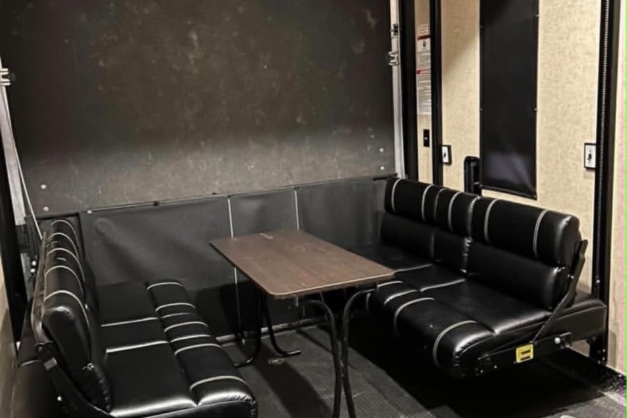 This RV rental interior features black cushioned benches with a table, forming a versatile dining/lounge area within a toy hauler.