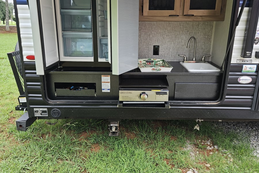 RV rental outdoor kitchen with open fridge, sink, and Greystone stove. Perfect for meals under the awning.