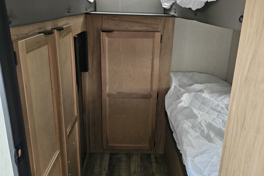 Cozy rv rental interior featuring bunk beds with white bedding, wooden storage cabinets, and a window overlooking greenery.