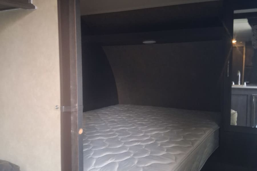 RV rental bedroom featuring a comfortable white mattress in a cozy nook, with a glimpse of the kitchen/bath.