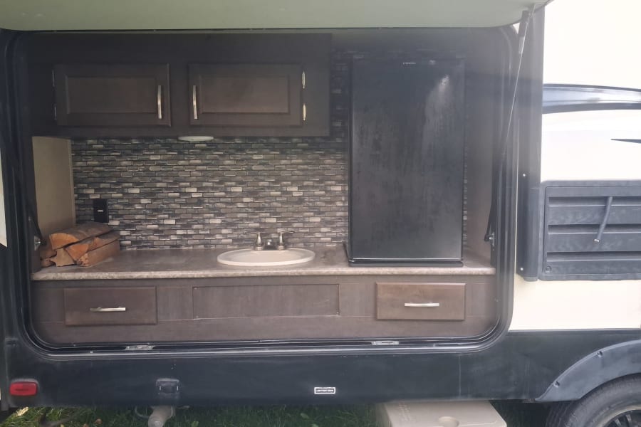 This RV rental outdoor kitchen features a sink, mini-fridge, cabinets, and a stylish backsplash for convenient camping.