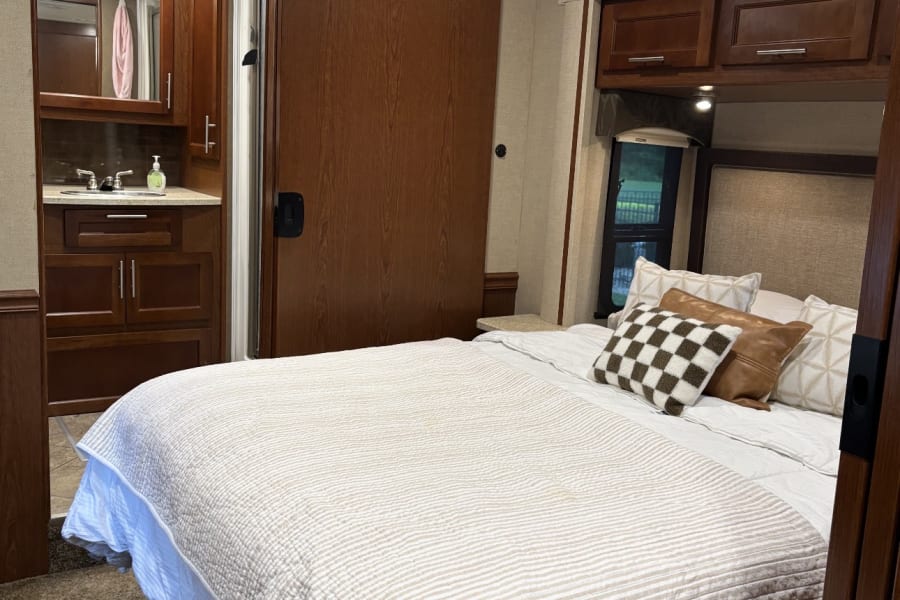 Cozy RV rental bedroom featuring a striped bed, decorative pillows, and an attached compact bathroom vanity.